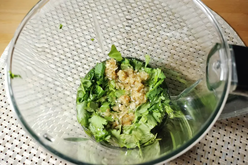Todos los ingredientes necesarios en el vaso de una batidora para hacer mojo verde de cilantro.